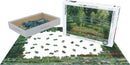 A jigsaw puzzle featuring Claude Monet's artwork 'The Japanese Footbridge'. The image shows the box with a vibrant painting of a serene footbridge surrounded by colorful flowers and lush greenery. The puzzle pieces are scattered around, with a partially completed puzzle on a white surface.