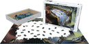 A jigsaw puzzle titled 'Soft Watch at Moment of First Explosion' by Eurographics. The puzzle features an art piece by Salvador Dali, with pieces scattered around a partially completed image showing surreal clocks and distorted landscapes. The puzzle box displays vibrant artwork and contains 1000 intricately shaped pieces for an engaging challenge.