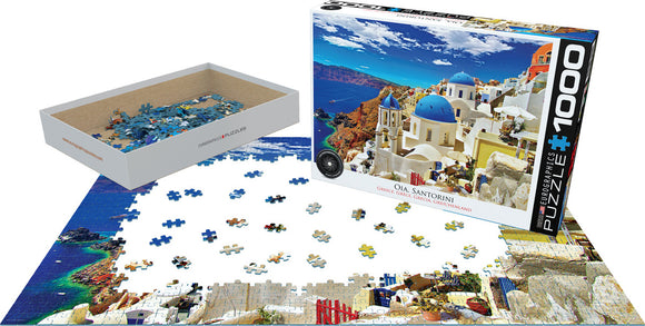 Eurographics jigsaw puzzle titled 'Oia, Santorini Greece' featuring 1000 pieces. The packaging shows a vibrant image of Santorini with blue domed roofs and stunning ocean views. A few scattered pieces are shown on a partially completed puzzle, demonstrating the delightful challenges of assembling this beautiful landscape.