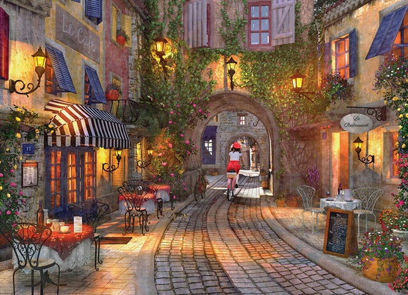 The French Walkway jigsaw puzzle featuring a picturesque French street scene with cafes, blooming flowers, and a cyclist riding through a quaint archway. Warm lighting illuminates the charming buildings adorned with colorful shutters and vines, inviting a sense of nostalgia and beauty.