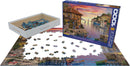 A 1000-piece jigsaw puzzle titled 'Mediterranean Harbor' by Dominic Davison, featuring a colorful coastal scene with boats, buildings, and a sunset. The pieces are scattered on a table, with the box displayed alongside.