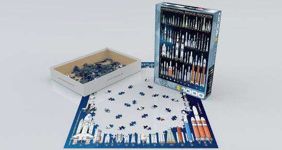 A jigsaw puzzle titled 'International Space Rockets' made by Eurographics. The image shows the opened puzzle box with various jigsaw pieces scattered, alongside the partially completed puzzle featuring different space rockets against a starry background. The puzzle includes 1000 pieces.