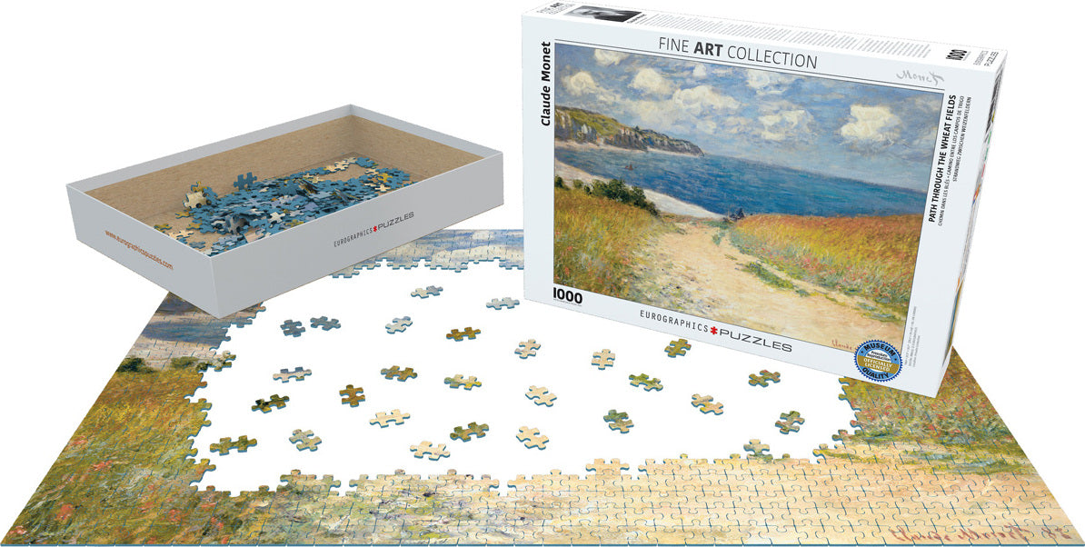 The jigsaw puzzle titled 'Path through the Wheat Fields' by Eurographics features a scene inspired by Claude Monet. The image showcases an opening box with puzzle pieces and a partially completed jigsaw laid out, revealing vibrant colors of golden wheat and a serene body of water under a blue sky. This 1000-piece puzzle is part of the Fine Art Collection.