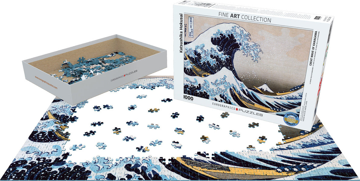 The Great Wave off Kanagawa jigsaw puzzle by Eurographics features a partially completed 1000-piece puzzle laid out on a flat surface. The box showcases a vibrant depiction of Hokusai's iconic woodblock print, with large waves crashing and Mount Fuji in the background. A tray beside it holds scattered puzzle pieces, emphasizing the intricate details and colors of the artwork.