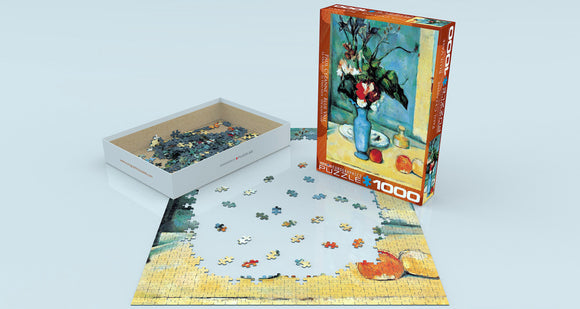A 1000-piece jigsaw puzzle titled 'Blue Vase' by Paul Cezanne, designed by Eurographics. The puzzle is partially completed on a light surface, with scattered pieces nearby. The packaging features an image of the artwork, showcasing a blue vase with flowers against a bright background.