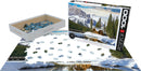 A jigsaw puzzle featuring a breathtaking winter scene of Yoho National Park in British Columbia. The image shows snow-capped mountains, evergreen trees, and a charming wooden cabin beside a serene lake. The puzzle consists of 1000 pieces and is packaged in a standard box with the image on display. Some puzzle pieces are scattered on a flat surface, demonstrating the progress of assembly.