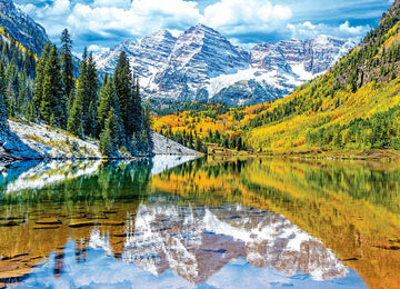 A vibrant jigsaw puzzle featuring the stunning Rocky Mountain National Park, showcasing majestic snow-capped peaks, lush green pine trees, and a serene lake reflecting the colorful autumn foliage. The image captures the beauty of nature with clear blue skies and fluffy clouds above the mountains.