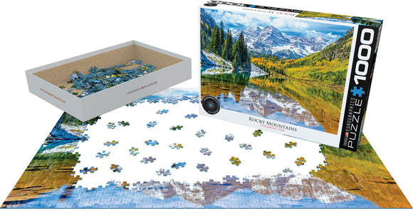 Eurographics Rocky Mountain National Park jigsaw puzzle featuring a stunning image of Colorado's Rocky Mountains. The puzzle includes 1000 pieces and is shown partially assembled, with pieces scattered around the box. The box displays vibrant colors of nature, including mountains, trees, and a reflective lake.