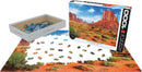 Eurographics Jigsaw Puzzle featuring Monument Valley, USA. The image shows the puzzle pieces scattered on a flat surface alongside the puzzle box, showcasing the dramatic red rock formations and vivid landscape.