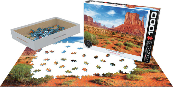 Eurographics Jigsaw Puzzle featuring Monument Valley, USA. The image shows the puzzle pieces scattered on a flat surface alongside the puzzle box, showcasing the dramatic red rock formations and vivid landscape.