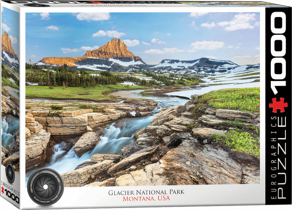 A beautifully illustrated jigsaw puzzle featuring the stunning landscape of Glacier National Park in Montana, USA. The image shows rocky formations, lush green meadows, and snow-capped mountains under a blue sky, capturing the essence of this natural wonder.
