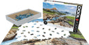 Eurographics 1000-piece jigsaw puzzle featuring a stunning landscape of Glacier National Park, Montana. The image showcases rocky formations, lush greenery, and scenic hills under a clear blue sky. The puzzle is displayed partially assembled, with scattered pieces visible in a white storage box.
