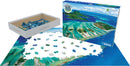 Eurographics Coral Reef jigsaw puzzle featuring a vibrant aerial view of a coral reef and surrounding islands. The puzzle is 1000 pieces and displayed partially assembled, with many blue and green pieces scattered around a white surface. The puzzle box shows the complete image, highlighting the beautiful blues of the water and the greenery of the islands, part of the Save Our Planet collection.