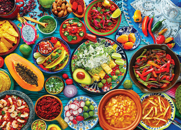 A colorful assortment of Mexican dishes displayed on a vibrant blue table. Items include tacos with cilantro and lime, fresh avocado, various dips like guacamole, and salsas alongside shrimp in a bowl, all surrounded by fruits and vegetables such as papaya, radishes, and various hot peppers.
