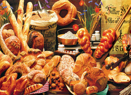 A colorful jigsaw puzzle featuring a bread table, displaying an assortment of breads including loaves, baguettes, and pastries arranged on rustic wooden surfaces with flowers, flour, and baking tools in the background.