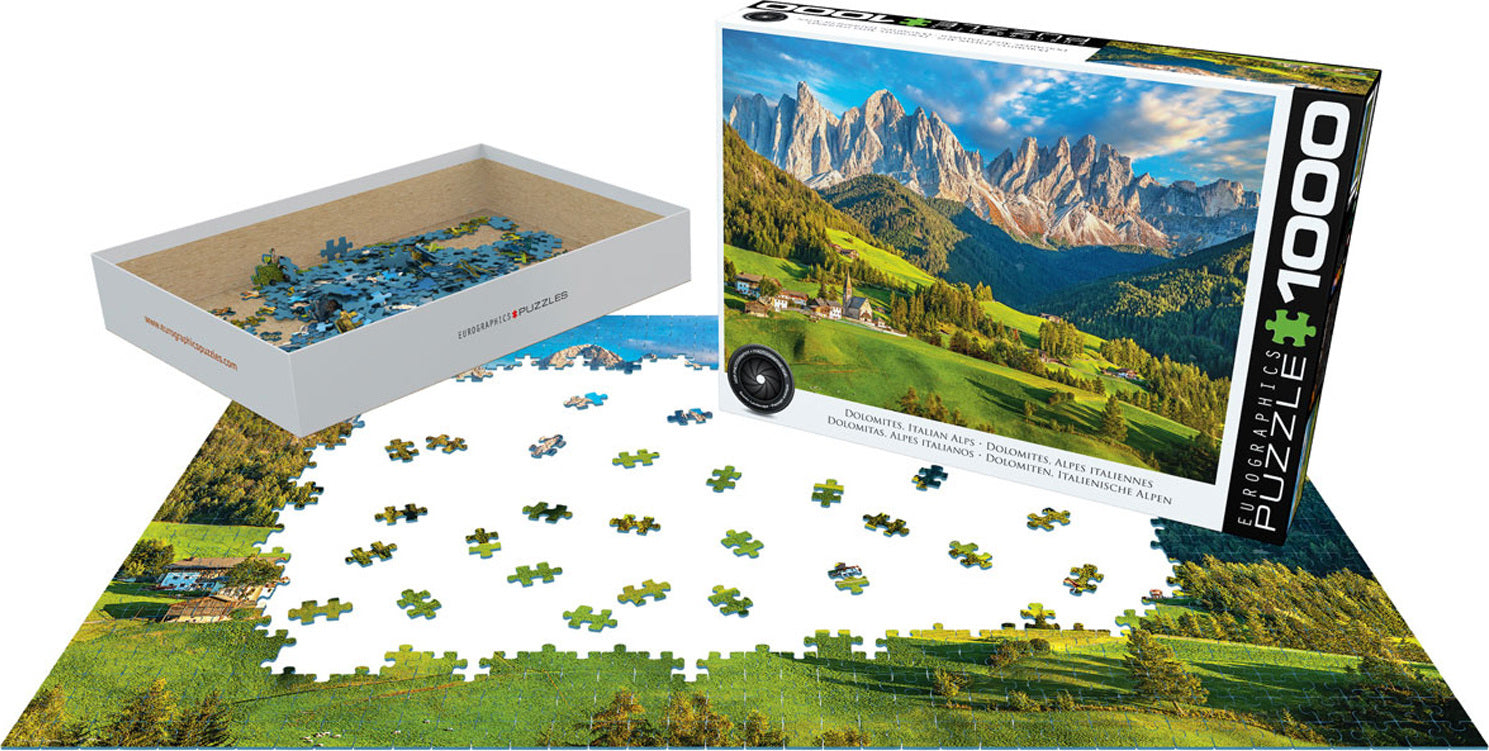 Eurographics 1000-piece jigsaw puzzle featuring a stunning panoramic view of the Dolomites in the Italian Alps. The puzzle pieces are scattered around, showcasing vibrant greens, majestic mountains, and quaint villages. The puzzle box displays the beautiful mountain landscape, highlighting the intricate details and colors, perfect for puzzle enthusiasts and nature lovers.