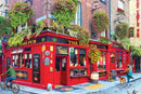 A vibrant street scene featuring 'The Irish Pub,' a colorful red-brick pub adorned with lush flower baskets and vintage signage. The pub showcases outdoor seating, a bicycle rider passing by, a woman walking her dog, and signs highlighting live music and traditional Irish culture.
