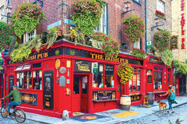 A vibrant street scene featuring 'The Irish Pub,' a colorful red-brick pub adorned with lush flower baskets and vintage signage. The pub showcases outdoor seating, a bicycle rider passing by, a woman walking her dog, and signs highlighting live music and traditional Irish culture.