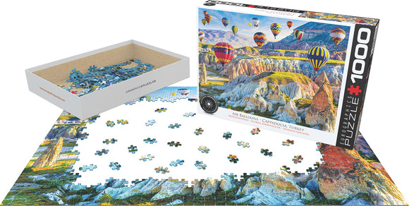 Air Balloons Over Cappadocia jigsaw puzzle by Eurographics featuring a vibrant scene of colorful hot air balloons ascending over the unique landscape of Cappadocia, Turkey. The image showcases the puzzle pieces scattered on a table alongside the puzzle box, highlighting the intricate details and colors of the artwork.