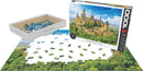 Hohenzollern Castle jigsaw puzzle by Eurographics. The image shows the puzzle pieces spread out on a table, with a partially completed image of the majestic castle surrounded by greenery. The box features a vibrant picture of the completed puzzle, showcasing the intricate architectural details of the castle and its scenic surroundings.