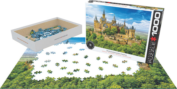Hohenzollern Castle jigsaw puzzle by Eurographics. The image shows the puzzle pieces spread out on a table, with a partially completed image of the majestic castle surrounded by greenery. The box features a vibrant picture of the completed puzzle, showcasing the intricate architectural details of the castle and its scenic surroundings.