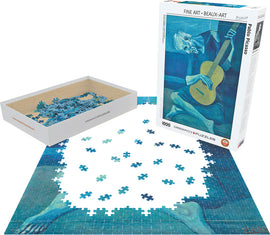 An intricate jigsaw puzzle of Pablo Picasso's 'Old Guitarist', showing several blue and gray pieces in a partially completed layout. The puzzle box sits nearby, displaying the artwork and details. This 1000-piece puzzle features the iconic image of an elderly man playing guitar, showcasing Picasso's signature style.