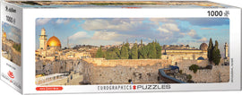 A beautifully designed jigsaw puzzle box titled 'Jerusalem' by Eurographics. The puzzle features a panoramic view of Jerusalem, showcasing the iconic skyline including the Dome of the Rock, and the Western Wall. The packaging highlights that the puzzle contains 1000 pieces and measures over 3 feet wide when completed. Ideal for puzzle enthusiasts and lovers of historical landscapes.