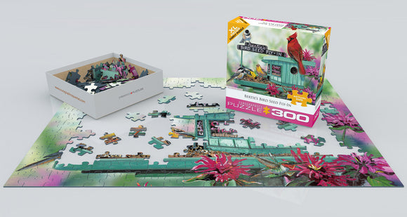 A vibrant jigsaw puzzle titled 'Bertie's Bird Seed Fly-In' from Eurographics. The image features colorful bird feeder surrounded by flowers, with puzzle pieces scattered around the partially completed scene and the puzzle box displayed nearby.