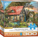 The Country Shed jigsaw puzzle by Dominic Davison, featuring a charming countryside scene with a quaint stone cottage, vibrant flower beds, and a wheelbarrow. The puzzle has 300 pieces and is designed for family fun. The packaging showcases the completed image and highlights its XL piece size for easy handling.