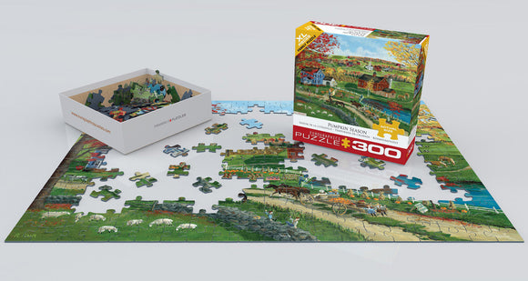 Eurographics Pumpkin Season jigsaw puzzle featuring a vibrant fall scene with colorful trees, a country landscape, animals grazing, and farmhouses. The puzzle is partially assembled, with pieces laid out on a white surface. The box design is visible, showcasing the illustration and the puzzle's title.