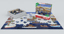 Seaside Holiday jigsaw puzzle by Carol Dyer, featuring a vibrant seaside scene with boats and people. The packaging shows the puzzle box next to scattered pieces on a partially completed image, designed for engaging family fun.
