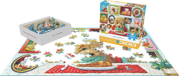 The Bon Appetit jigsaw puzzle by Eurographics is displayed with pieces scattered on a table. The image features a cute dog sitting at a table with a plate of food, surrounded by vibrant artwork depicting various dining scenes. The puzzle box is prominently shown, highlighting its colorful and engaging design, along with a tray of puzzle pieces ready to be assembled.