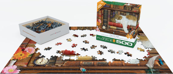 A colorful 500-piece jigsaw puzzle titled 'The Cat Nap' by Eurographics. The puzzle features a cozy scene with a sleeping cat on a stack of books, surrounded by flowers and a classic clock. The box is shown alongside pieces scattered on a partially completed puzzle on a flat surface.