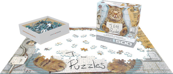 The Feline Felon jigsaw puzzle box by Eurographics rests next to a partially completed puzzle on a flat surface. The puzzle features a humorous image of a cat holding a sign that says 'I EAT Puzzles' against a playful background. The open box displays colorful puzzle pieces, while several pieces are scattered around the puzzle.