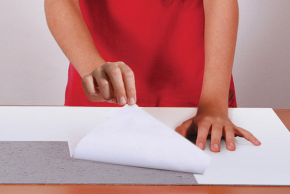 A person in a red shirt is applying Individual Smart Puzzle Glue S from Eurographics to a jigsaw puzzle, demonstrating its use for preserving completed puzzles. The glue is being smoothly pressed onto a puzzle piece on a flat surface, showing its adhesive properties.