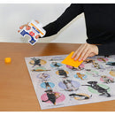 A person applying Eurographics Individual Smart Puzzle Glue on a completed jigsaw puzzle featuring various dogs. The glue bottle is in one hand, while the other hand holds a yellow smoothing tool, ensuring the pieces are secured together. The puzzle is laid out on a wooden table, showcasing colorful circular designs with different dog images.