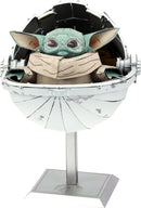ICONX: The Child is an intricate DIY kit by Metal Earth, featuring a detailed metal model of the beloved character from Star Wars, sitting inside a silver hover pod. The Child has large expressive eyes and is wrapped in a soft brown cloak, showcasing refined craftsmanship and engineering in miniature form.