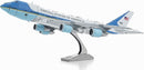 A detailed metal model of Air Force One, showcasing its iconic blue and white color scheme, with the words 'United States of America' on the fuselage. The model is displayed on a sturdy base, highlighting the aircraft's sleek design and three prominent engines.