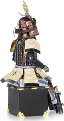 A detailed DIY kit of a Metal Earth Samurai Armor model showcasing intricate metal pieces. The model features a traditional samurai helmet adorned with a golden crest, layered armor plates, and a striking pose. The craftsmanship highlights various textures and colors, including bronze, silver, and black, suitable for hobbyists and collectors.