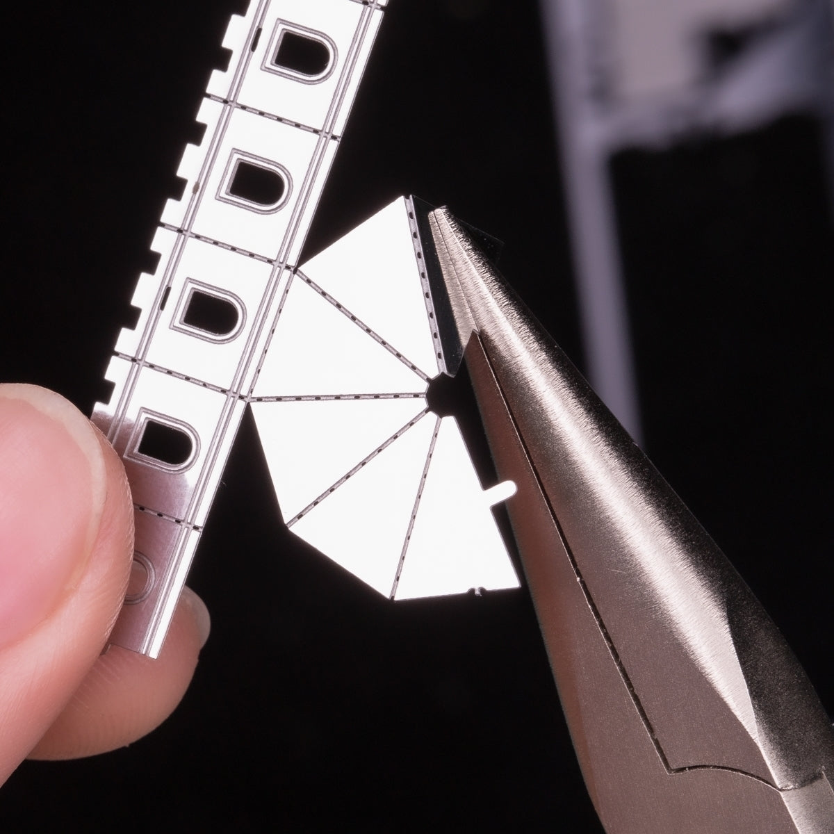 A close-up image of a hand holding a precision tool, delicately interacting with a metal piece featuring intricate cut designs. The metal has a shiny, reflective surface, showcasing fine detail and craftsmanship, ideal for enhancing DIY projects.