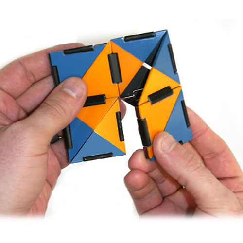 A person holding Ivan's Hinge, a colorful mechanical puzzle made by Fat Brain Toys. The puzzle features interlocking geometric shapes in blue, orange, and black. It challenges users to manipulate the pieces into various configurations, promoting problem-solving skills and fine motor development.