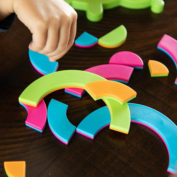 A close-up of brightly colored pieces from the Bugzzle game by Fat Brain Toys, featuring various shapes and a child's hand reaching for a piece. The game includes vibrant green, blue, pink, and orange components designed for engaging play.