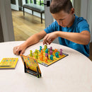 A young boy focused on playing 'Zoo Rendezvous,' a mechanical puzzle by Fat Brain. The colorful game features various animal-shaped pieces on a vibrant game board, alongside a challenge booklet. The scene is set on a light wooden table with natural lighting, highlighting the boy's concentration as he maneuvers the pieces.