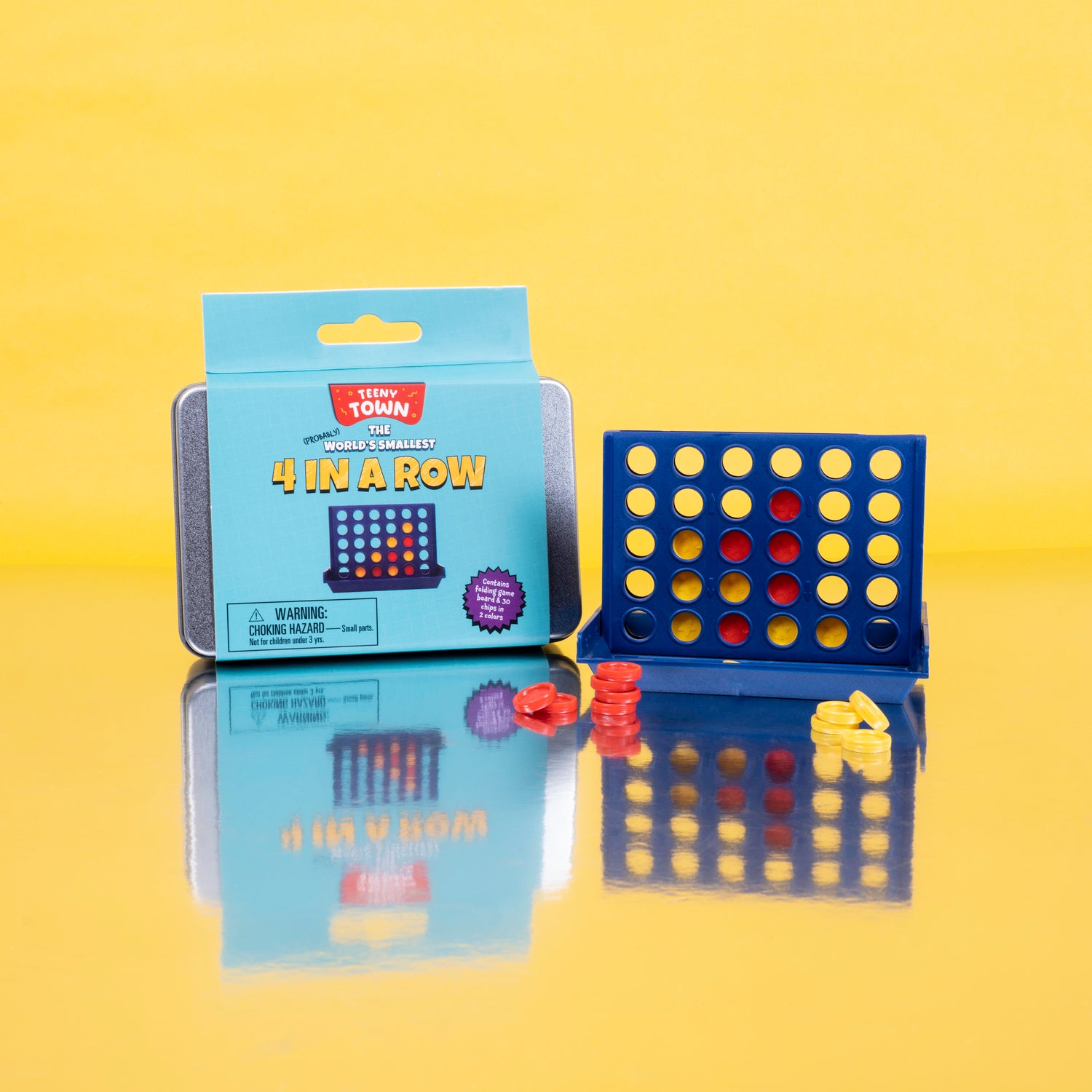 Teeny Town 4 in a Row game by Fizz Creations Inc. shows a compact game board with colorful slots and circular tokens in red and yellow. The partially-opened packaging highlights its size as the world's smallest 4 in a row game, set against a bright yellow backdrop.