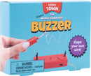 The Teeny Town Buzzer Game, a playful DIY kit from Fizz Creations Inc., features a hand holding a mini buzzer with a vibrant red casing and wire. The packaging is light blue with the words 'The World's Smallest Buzzer' and a warning about choking hazards. A purple starburst encourages users to 'shape your own wire!'
