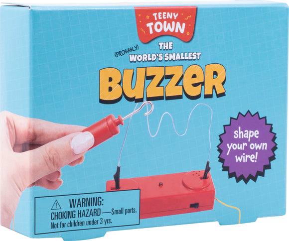 The Teeny Town Buzzer Game, a playful DIY kit from Fizz Creations Inc., features a hand holding a mini buzzer with a vibrant red casing and wire. The packaging is light blue with the words 'The World's Smallest Buzzer' and a warning about choking hazards. A purple starburst encourages users to 'shape your own wire!'