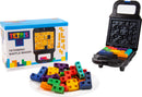 A Tetris Waffle Maker by Fizz Creations Inc. is displayed upright, with colorful Tetrimino-shaped waffles piled on a white plate beside it. The waffle maker is partially open, showcasing the vibrant waffles inside and the branded box in the background, featuring the iconic Tetris logo and colorful design.