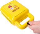 A vibrant yellow Pac Man Waffle Maker featuring the iconic Pac Man character and colorful ghosts on the lid. The waffle maker is designed to create fun Pac Man-shaped waffles, perfect for fans of the classic game. A hand is shown pulling the handle, indicating its use.