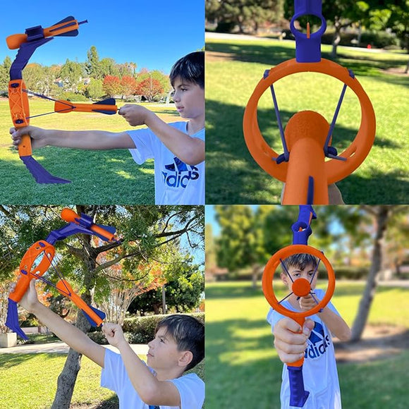 A young boy demonstrates the Mighty Strike game by Funwares in a park. The boy is aiming the colorful, orange and purple toy that resembles a slingshot with a round target holder. The background features green trees and a clear blue sky, emphasizing a fun outdoor play environment.