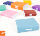 A collection of colorful miniature books in various shapes and sizes, displayed on a light background. The books feature different colors including blue, pink, orange, and purple, each with simple designs on their spines, making them visually appealing and fun for display or use in activities.
